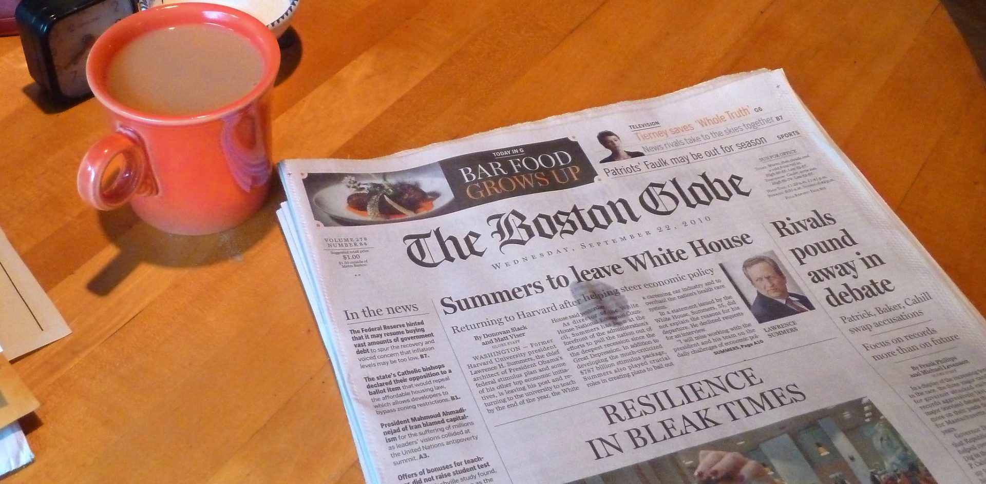 A cup of coffee with the Boston Globe newspaper with the headline Resilience in Bleak Times. Photo by Liz West