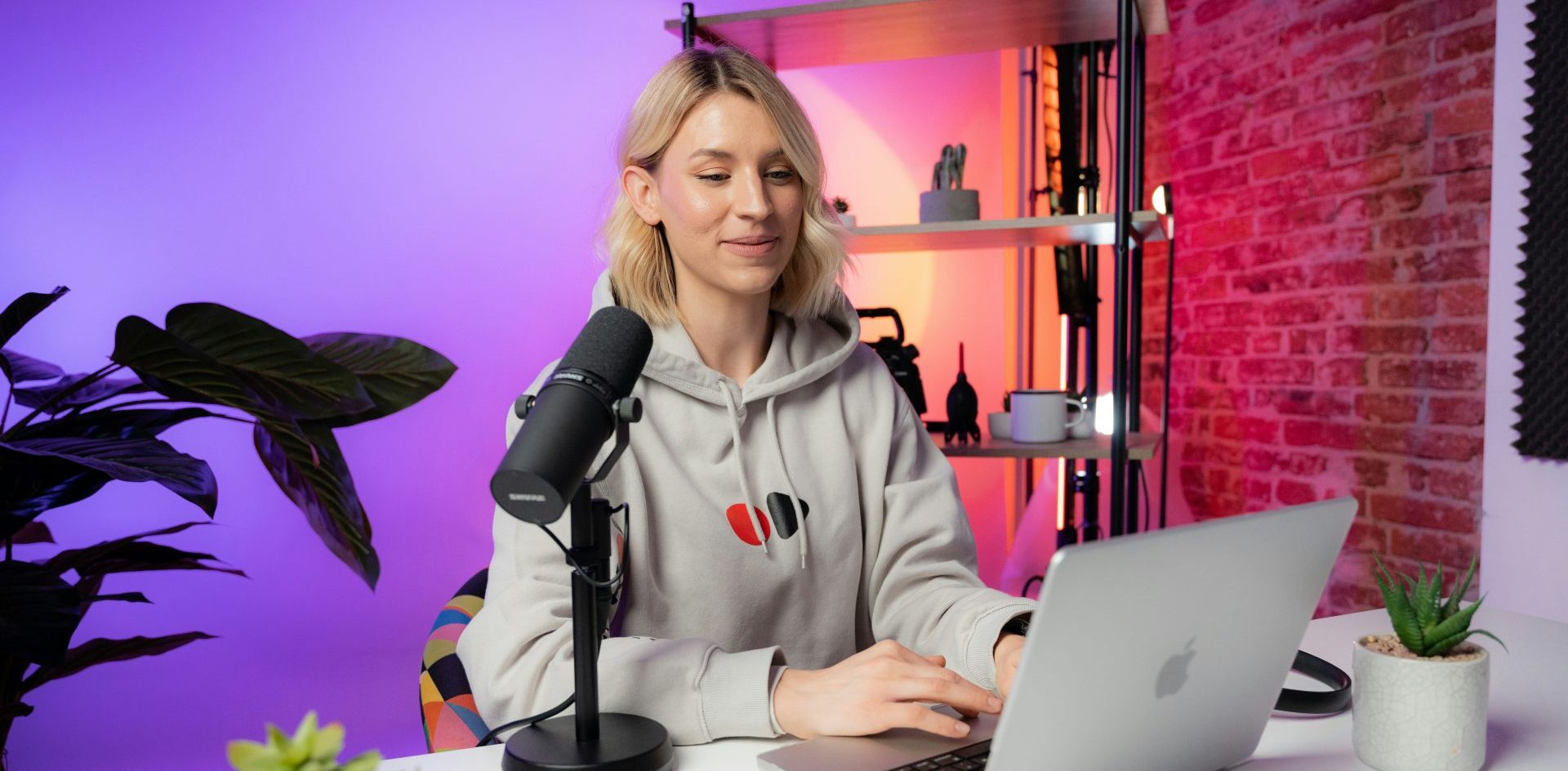 A woman sits in behind a microphone and a laptop in a studio. Photo Videodeck .co on Unsplash