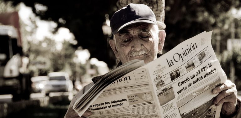 A man reads a newspaper along a street. By Kmilo . from Santiago, Chile - Relajo, CC BY 2.0