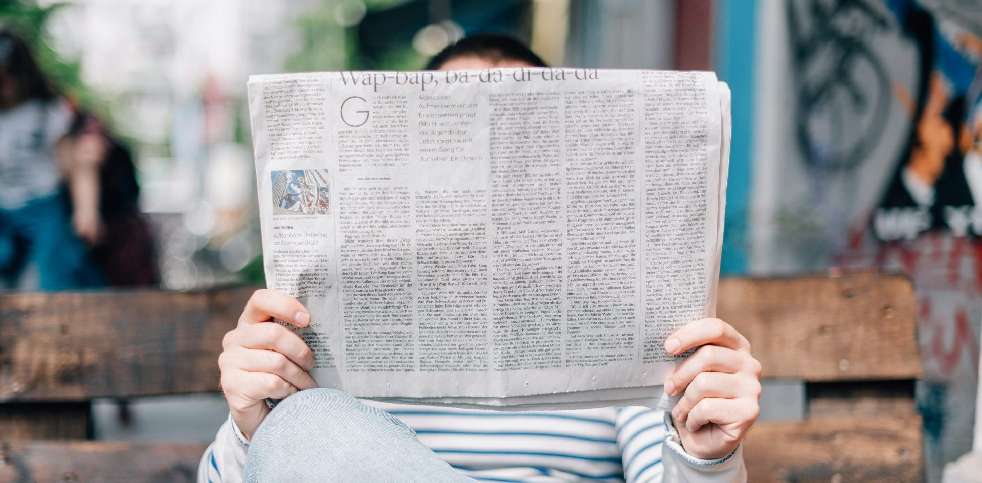 A man sits on a park bench reading a newspaper. Photo by Roman Kraft from Unsplash